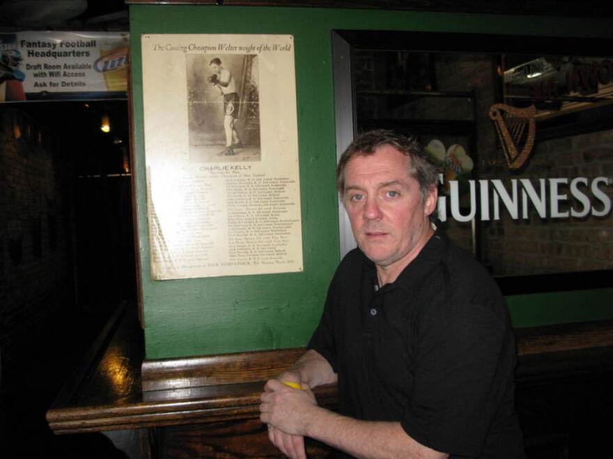 Michael Harvey stands next to a poster of his great-great-uncle Charlie Kelly at his Lincoln Park bar. Harvey's main character, Michael Kelly, was named after Charlie's father.