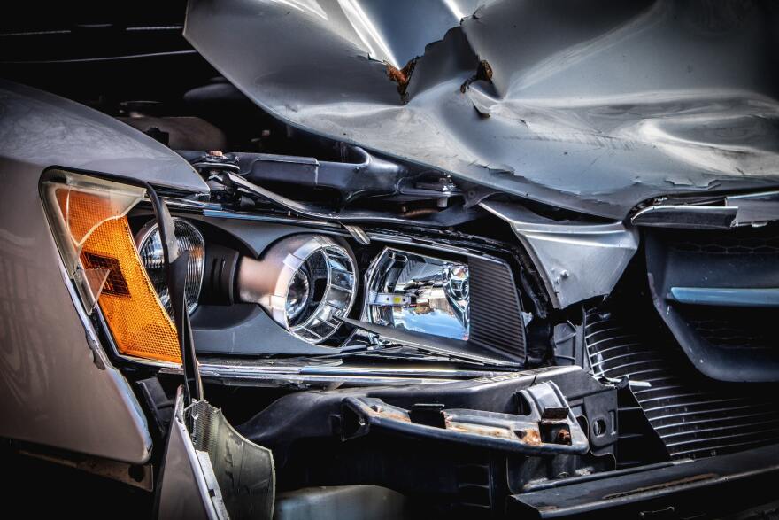 A car with its front hood smashed and caved in, revealing a silver and black car engine