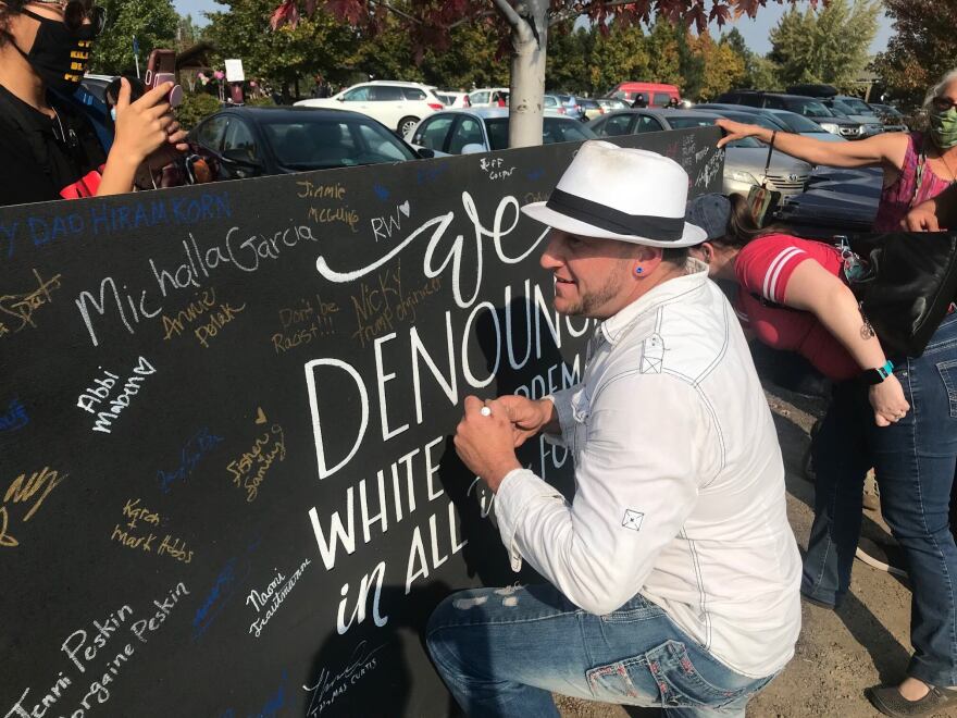 Nicholas Dieringer signs a board denounce white supremacy in Bend on Oct. 3, 2020, after planning a pro-Trump rally in the same park as a picnic hosted by racial justice groups.