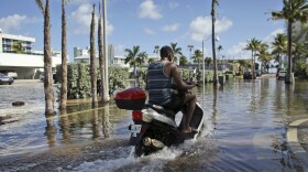 A motorbike navigates through floodwater caused by a seasonal king tide, Monday, Oct. 17, 2016, in Hollywood, Fla. King tides bring in unusually high water levels and can cause local tidal flooding.