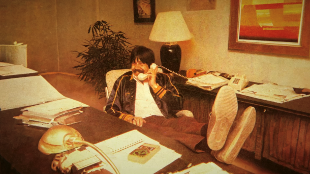 Throwback photo of David Marsden at a desk with his feet up, talking on a landline phone.