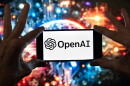 The OpenAI logo is displayed on a cell phone in front of an image generated by ChatGPT's Dall-E text-to-image model, Dec. 8, 2023, in Boston.