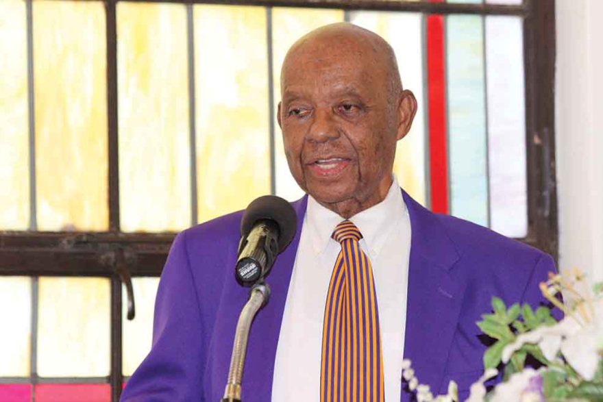 Older bald Black man in a blue sportcoat and tie and speaking into the camera