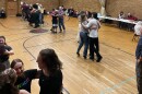 A school gym with people dancing, arms around each other in groups of three