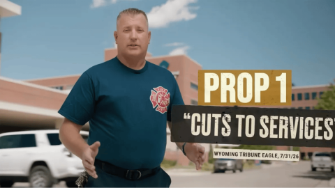 A men wearing a shirt with a logo of a fire department stands in front of a building. Words are superimposed over the image reading, "Prop 1 'Cuts to services' Wyoming Tribune Eagle, 7/31/26."