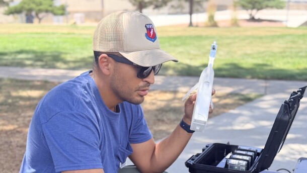 Juan Hernandez, a man wearing a blue T-shirt, green pants, and a tan ball cap, sits in front of a laptop computer outside. He is an incident meteorologist with the National Weather Service, uses a radiosonde while working near the Aspen Acres Fire in southern Colorado on Tuesday. A radiosonde measures temperature, relative humidity, wind and pressure.