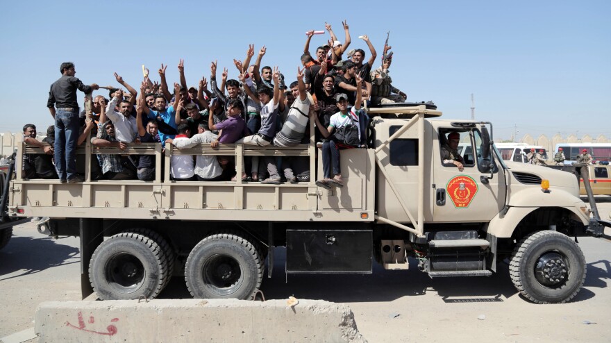 Iraqi men flash victory signs as they leave the main recruiting center to join the Iraqi army in Baghdad on Tuesday.