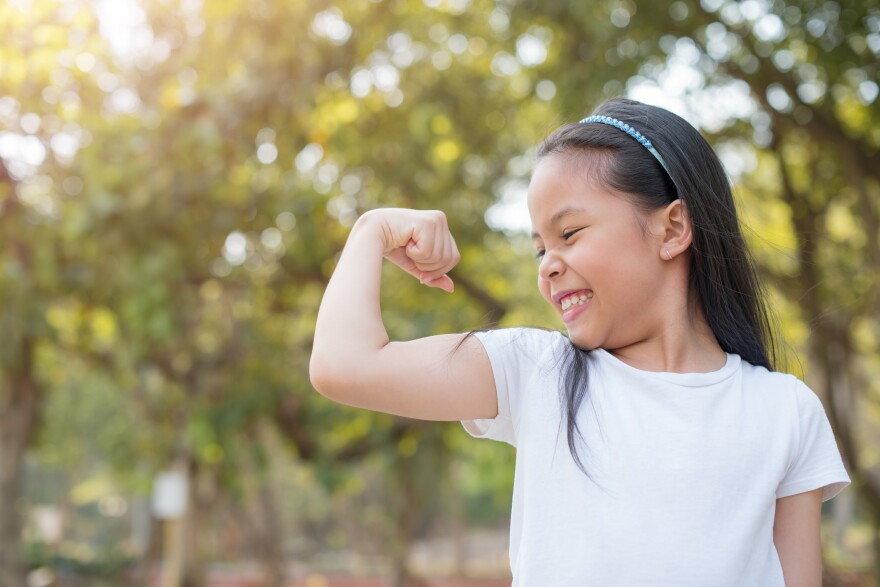 happy little girl child proudly flexing her biceps while playing outdoors