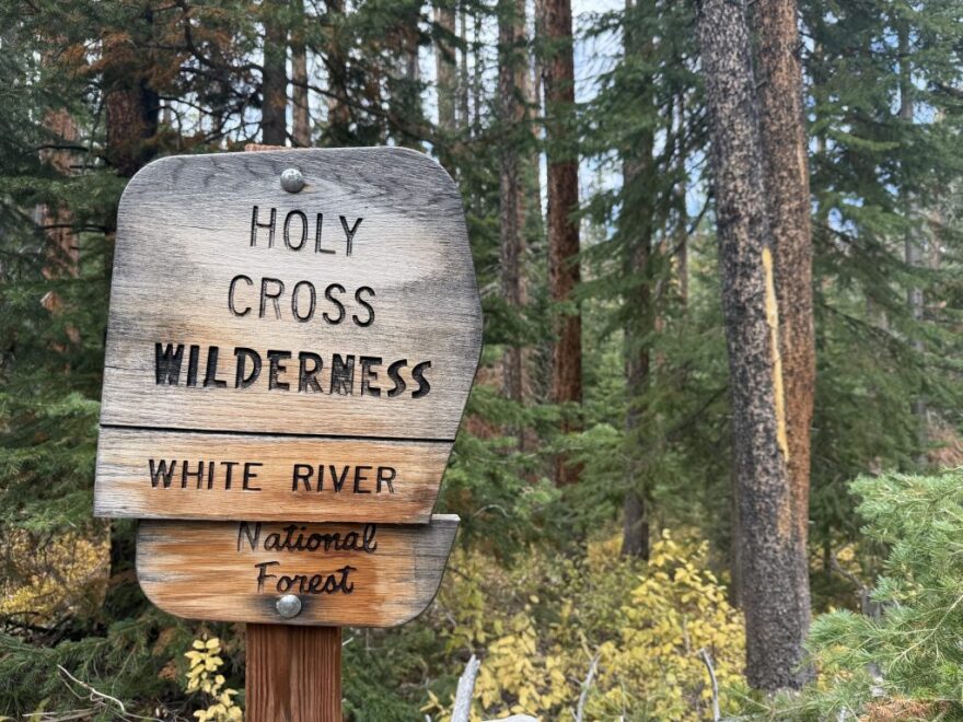 A sign that shows "Holy Cross Wilderness" in front of a forest.