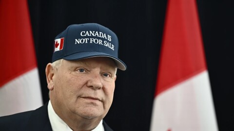Ontario Premier Doug Ford stands wearing a "Toronto Is Not For Sale" hat, with multiple Canadian flags in the background.