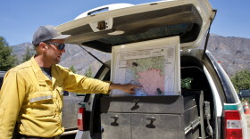 A man in a yellow jacket point  to a map in the back of a truck. 