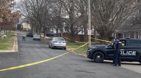 Police car parked next to a city street that is surrounded by police tape and has several cars parked on the side of the one way street