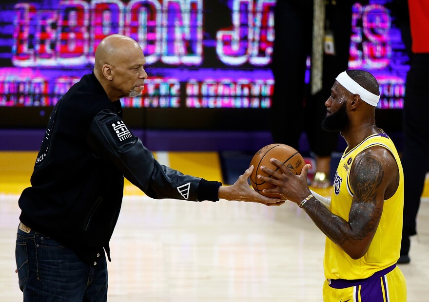 Kareem Abdul-Jabbar (left) hands LeBron James a basketball celebrating James' all-time NBA scoring record Tuesday night in Los Angeles.