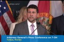 A brown haired man in a gray suit and lavender tie speaks at a microphone