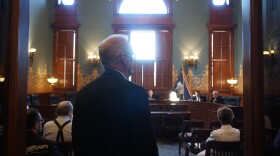 A man looks into a room full of people with a bright window in the back.