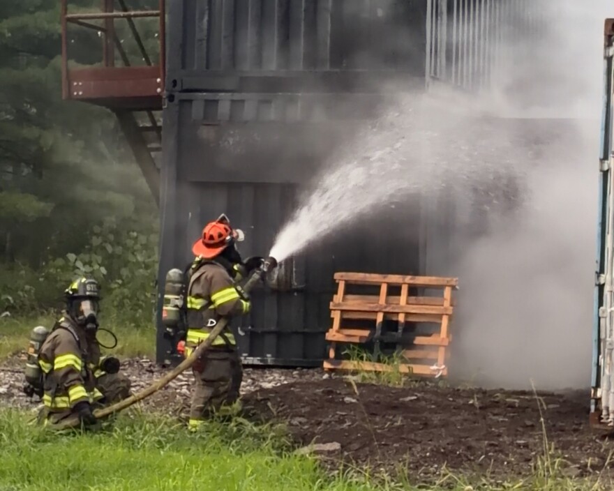 two firefighters hold a hose that is shooting water towards a burning structure