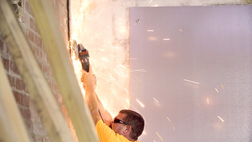 Chris Thomas uses an angle grinder to cut nails from the Bedford Collab walls.