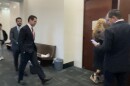 James Fishback, wearing a suit, walks down a courthouse hallway toward a courtroom door, accompanied by others in business attire.