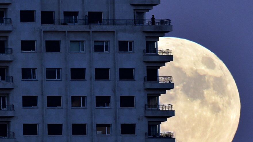 With the Nov. 13 supermoon rising in the background, a man looks out from a balcony in Madrid. At its closest pass to Earth, the full moon can look up to 14 percent bigger and 30 percent brighter, NASA says.