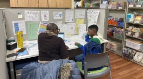 A child sits with his reading tutor at a desk in a room surrounded by bookshelves and reading posters at UW-Milwaukee.