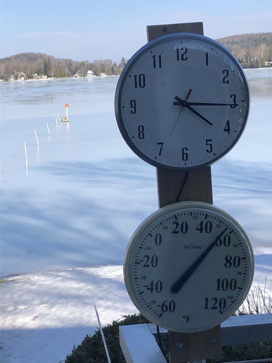 A thermometer and clock is pictured near a frozen lake.