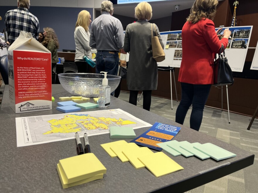 Green and yellow sticky notes and black permanent markers sit on a table. In the background, people inside Arlington City Council chambers go from board to board to learn about proposed Arlington missing middle and infill development housing policies.