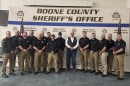 Men in black shirts and khakis pose in front of Boone County banner