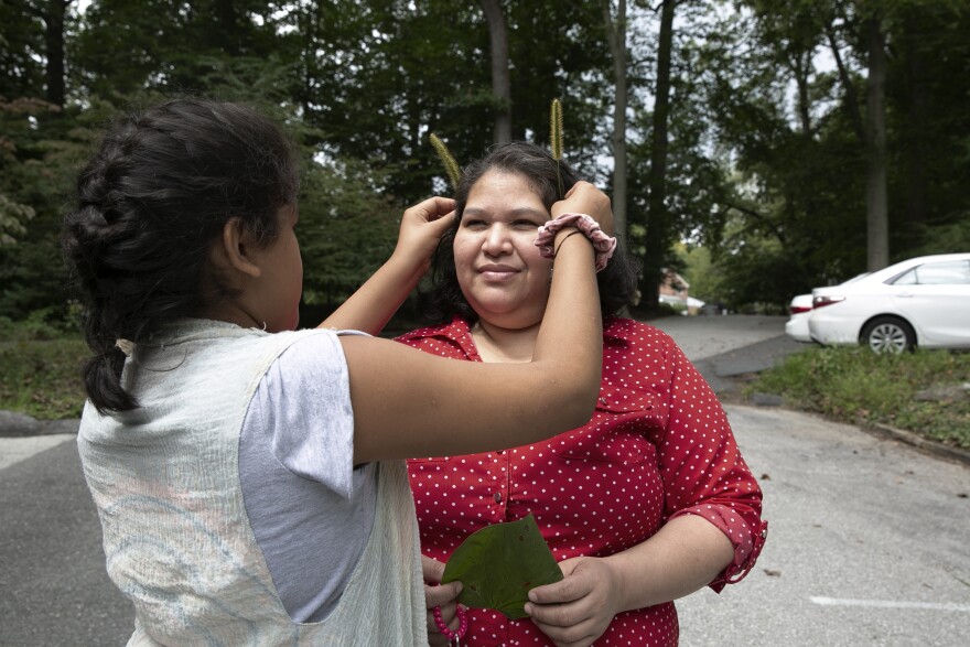 Maria puts green foxtails on Rosa's head.