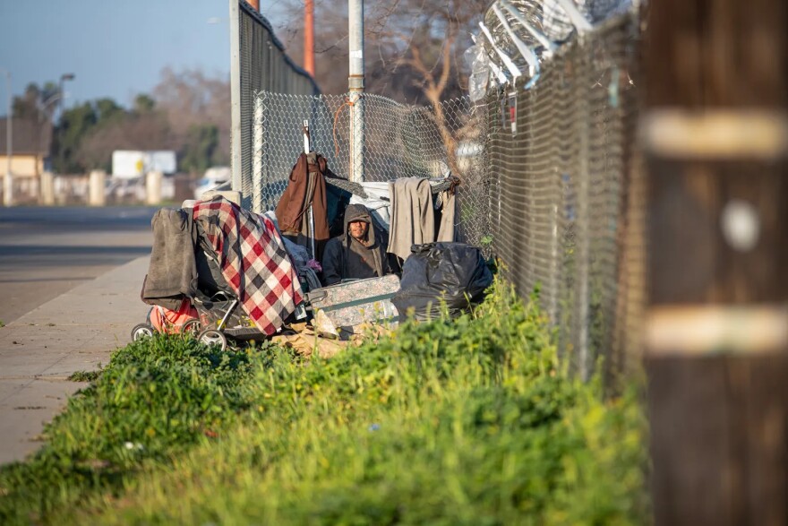 A person sits in a makeshift tent along a barbed wire fence near Highway 99 in southwest Fresno on Feb. 11, 2022.