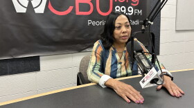 A woman speaks into a radio microphone in front of a WCBU 89.9 FM banner.