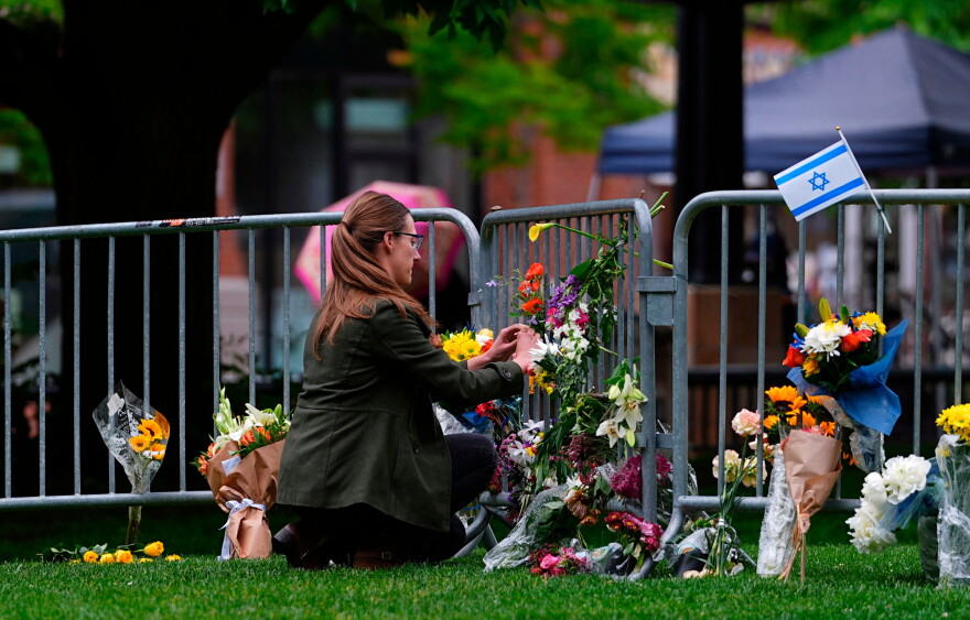 A woman places a bouquet of flowers along a guardrail where other flowers have been left.