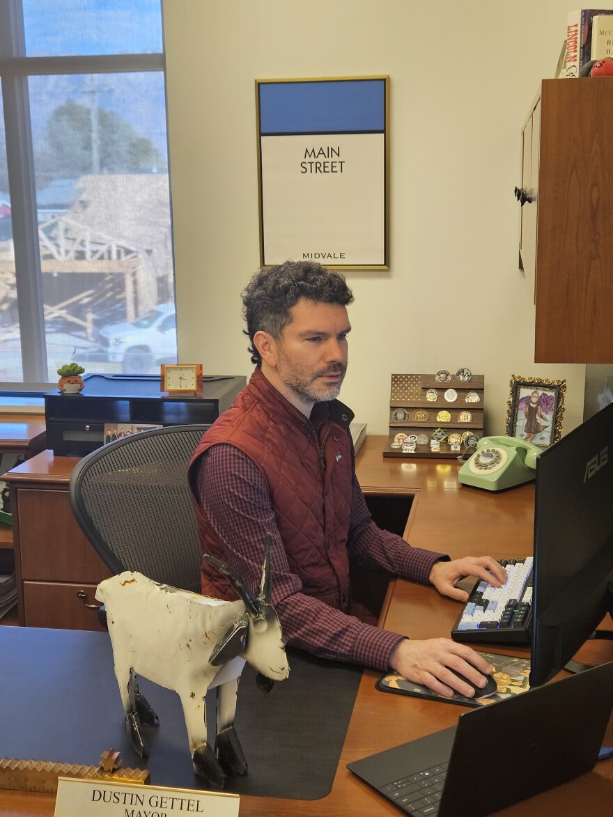 A person in a red vest uses a desktop computer, beside a white statue of a goat.