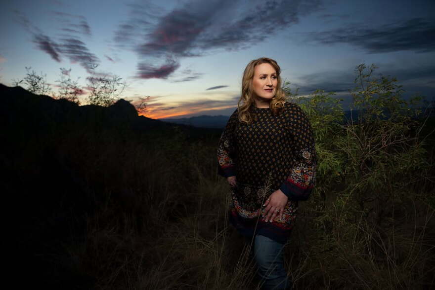 Woman in black shirt with blonde hair poses in front of mountain at sunset
