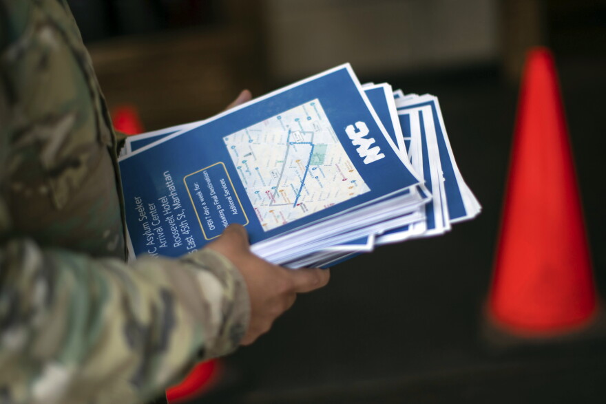 A military member carries flyers for asylum seeking migrants as they arrive to the Roosevelt Hotel in New York.