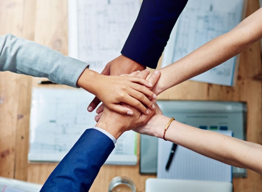 Five arms outstretched with hands meeting in the middle on top of each other; below are some work papers and documents