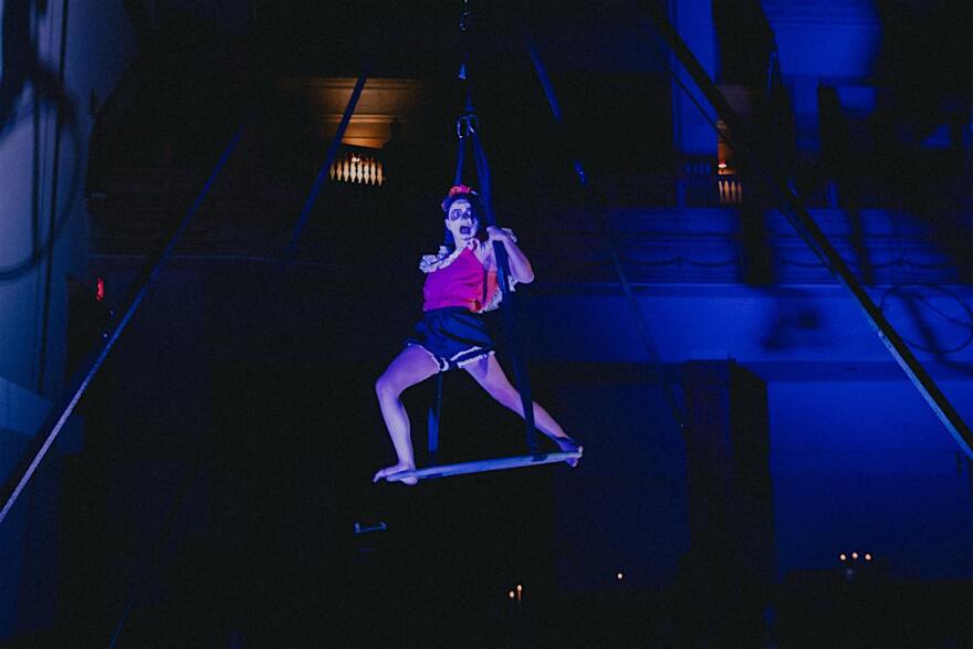 Performer in the dark hangs above the ground with a support. 