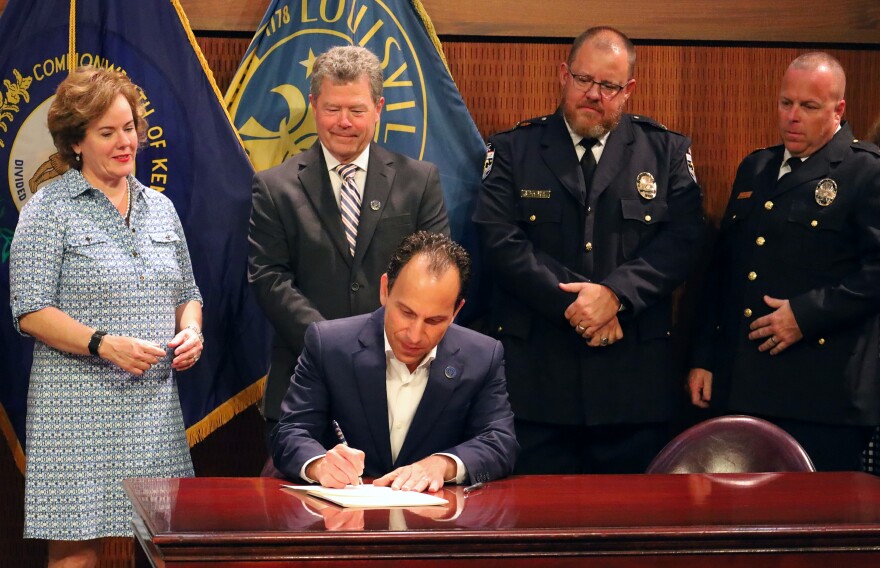 Louisville Mayor Craig Greenberg signing the new ordinance into law while surrounded by city officials.