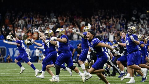 Washington players in purple uniforms running on to the field celebrate victory against Texas.