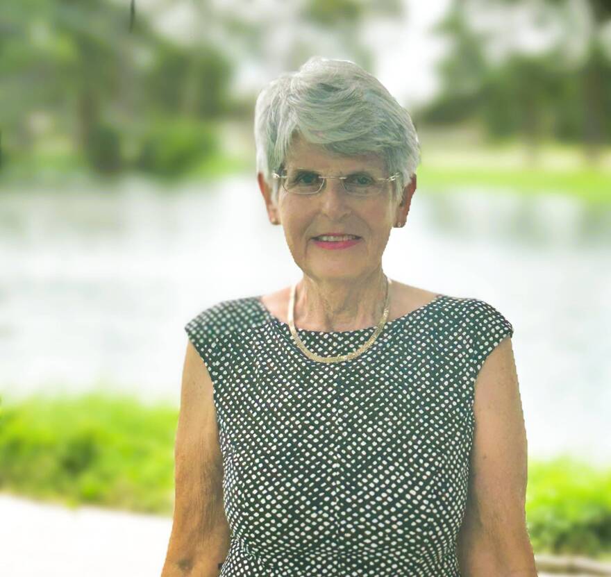 Older woman in a dress smiles at camera outside 