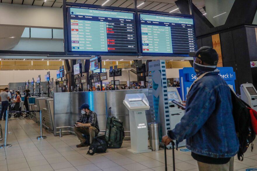 A passenger holds his mobile phone while looking at an electronic flight notice board displaying canceled flights at OR Tambo International Airport in Johannesburg, South Africa.