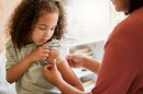 A child looks at her left arm as a medical professional smooths out a bandage