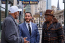 Three men in professional jackets stand outside in downtown Detroit. The man pictured in the middle, in a blue jacket, is Abdul El-Sayed. 