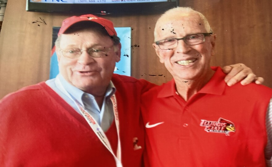 Two men in red shirts stand together for a picture
