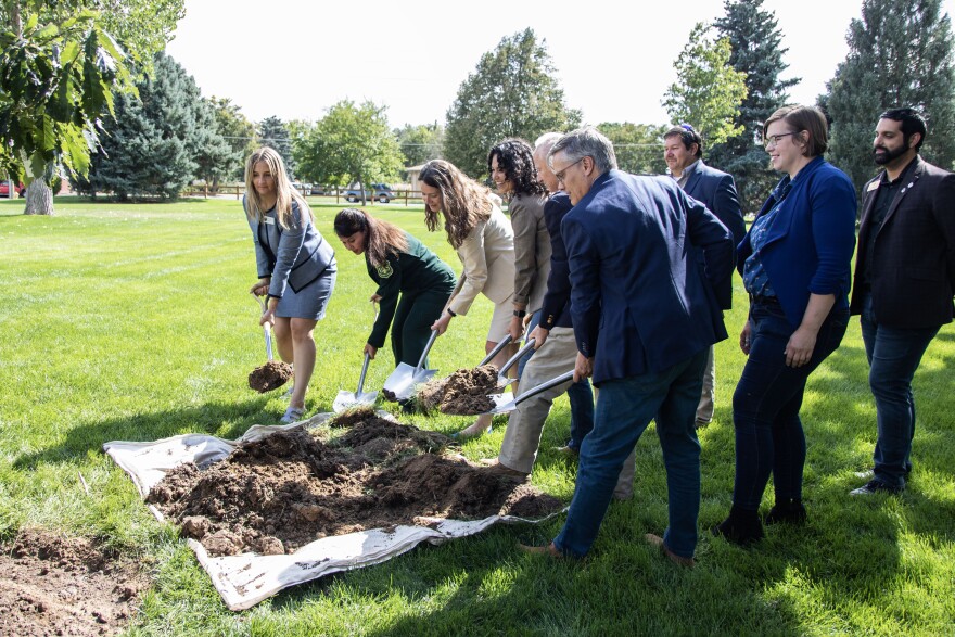 Xochitl Torres Small, the deputy secretary for the U.S. Dept. of Ag., and a group of people gather and dig shovels into a small mound of dirt surrounded by trees and green space