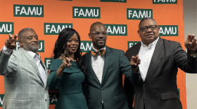 Four people standing before a green-and-orange backdrop with "FAMU" printed on it