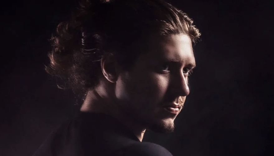 A man with a goatee and hair in a bun is staring off into the distance