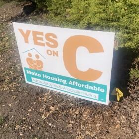 A sign standing in dirt reads "Yes on C. Make housing affordable." 