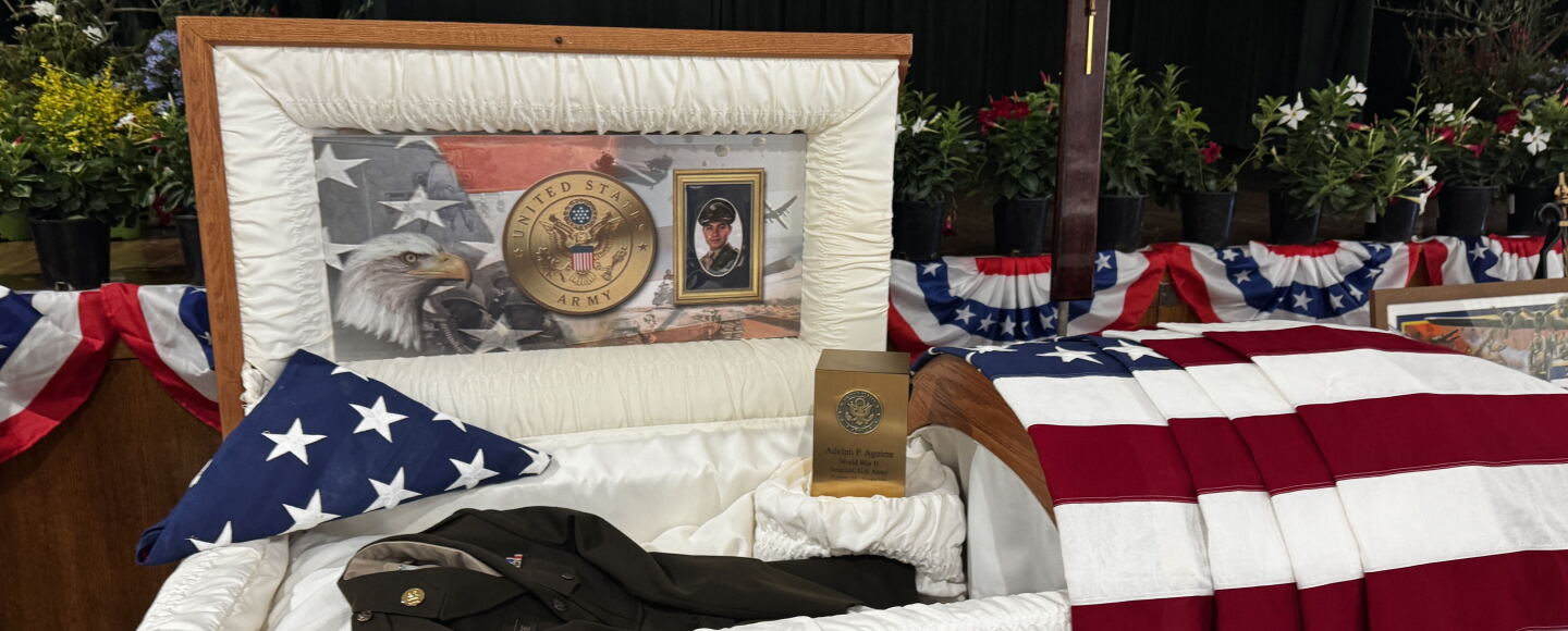 Casket with photos of Sgt. Adolph Aguirre and his uniform. American flag draped over. 