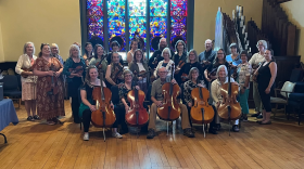 The Marquette County String Orchestra Society in a group photo with their instruments. The front row is sitting with cellos, and the back row is standing with violins and violas.