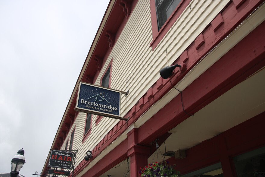 A navy sign reads "Breckenridge Mountain Massage" with a mountain logo on a red and cream building. A light is pointed at it from the side.